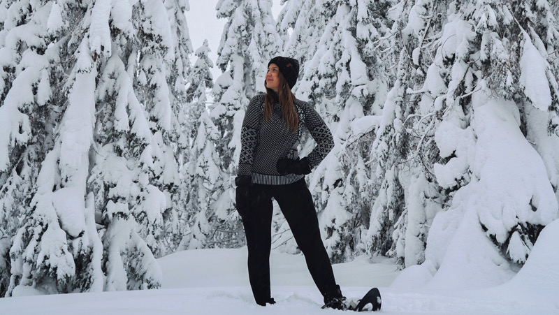 Snowshoeing in snowy tree forest wearing merinowool layers by Erika Katainen